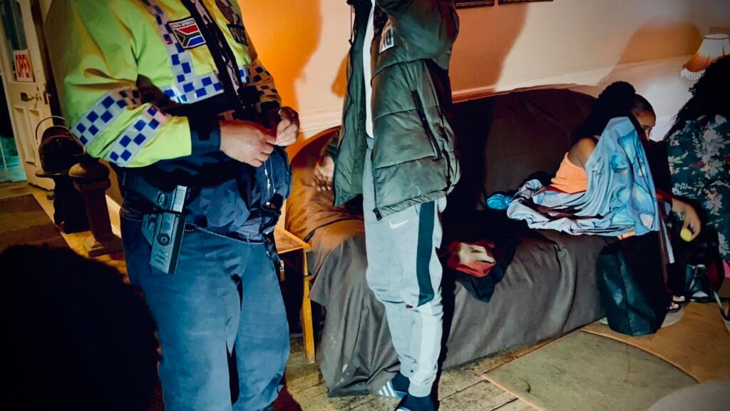Phoenix man caught during Durban massage parlour raid stands beside woman hiding face on couch